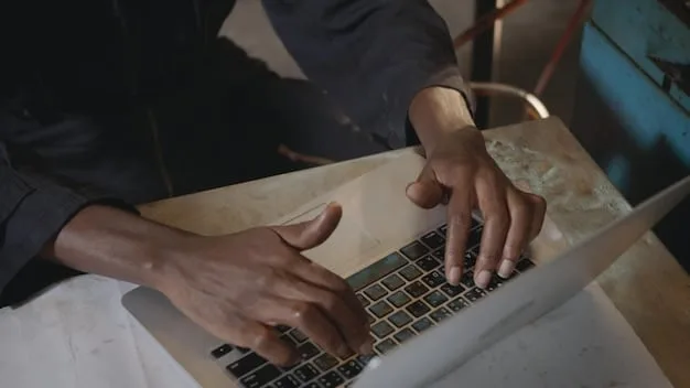 A close-up shot of a young Gen Z individual’s hands typing on a very old, slow, and visibly struggling laptop, demonstrating the challenge of device inequity in an underserved setting.