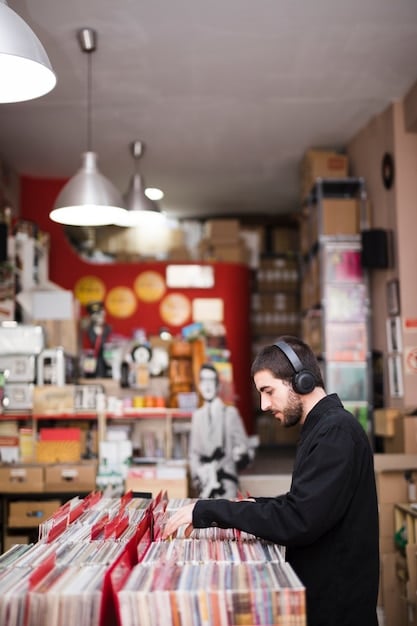 A brightly lit record store with diverse vinyl albums on display. Various Gen Z individuals are browsing through the records, some holding albums and examining them closely. The store has a vintage aesthetic with posters of classic musicians and bands adorning the walls.
