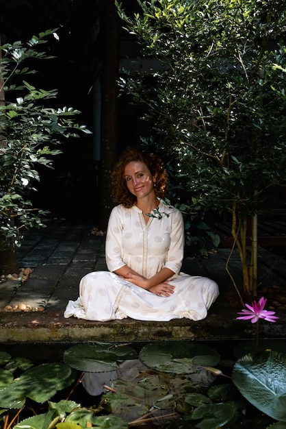 A serene image of a young person meditating in a quiet, natural setting, surrounded by green plants and soft lighting. Their eyes are closed, and their expression is peaceful and relaxed.