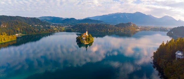 A stunning panoramic view of Lake Bled in Slovenia, with its iconic island church and castle, bathed in soft morning light, showcasing its natural beauty and inviting adventurous exploration.