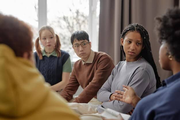 A school counselor talking empathetically with a diverse group of teenagers, one of whom identifies as gender non-conforming, in a brightly lit and modern school office setting with supportive posters on the wall.