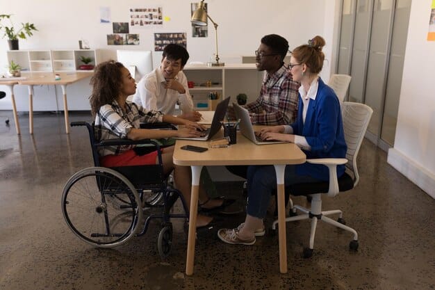 A diverse group of young adults, some with physical disabilities, working collaboratively in a modern office environment, symbolizing the long-term societal impact of inclusive education.
