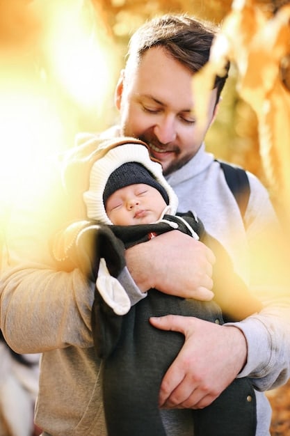 A father gently holding his 4-month-old baby, who is looking up at him with a wide, happy smile and bright, engaged eyes, both seemingly enjoying a quiet, joyful moment of connection.